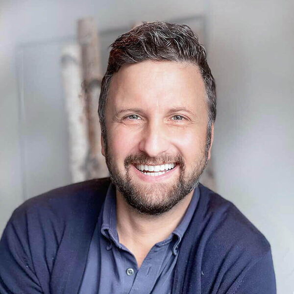 Ein lächelnder Mann in einem blauen Hemd und Pullover strahlt Freude aus.