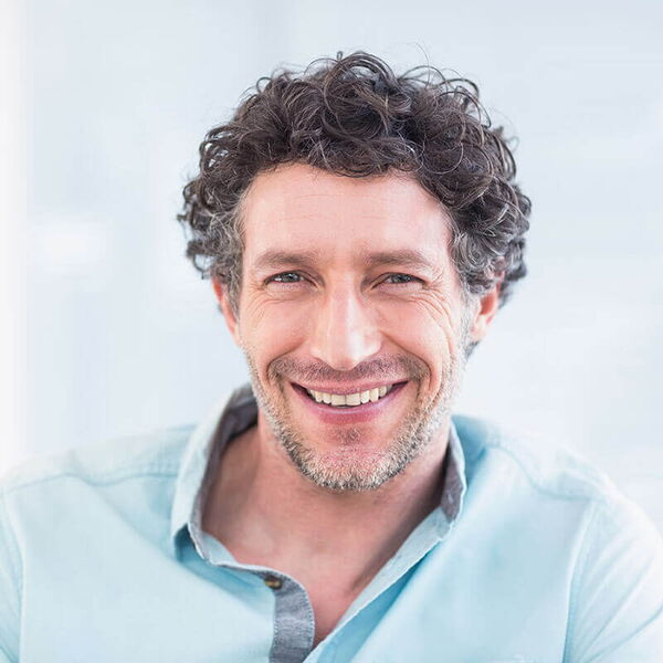 Ein lächelnder Mann in einem hellblauen Hemd blickt freundlich in die Kamera.